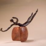 Abstract wooden sculpture of a reclining human figure on a rounded base.