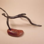 Abstract metal sculpture of a figure on a wooden base.